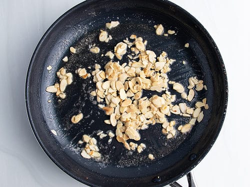 Overhead view of a large non-stick skillet with melted butter and thinly sliced raw almonds.