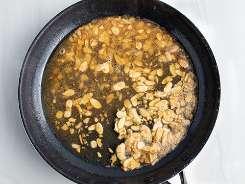 Overhead view of chicken almondine sauce (butter, chicken broth, lemon juice, and almonds) in a large black non-stick skillet.