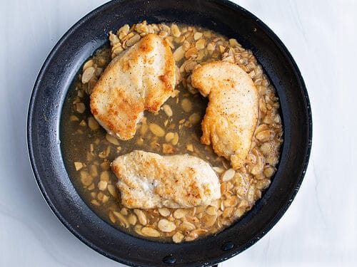 Overhead view of chicken almondine in a large black non-stick skillet.