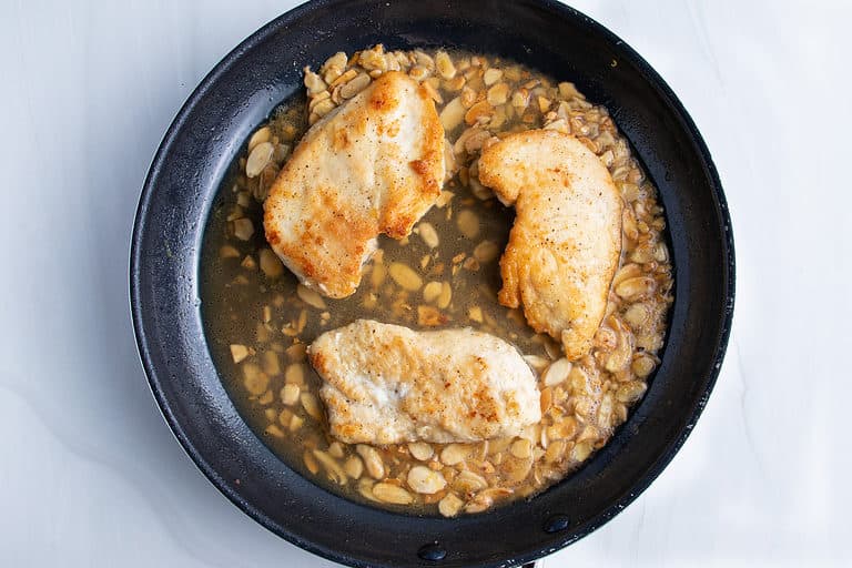 Overhead view of chicken almondine in a large black non-stick skillet.