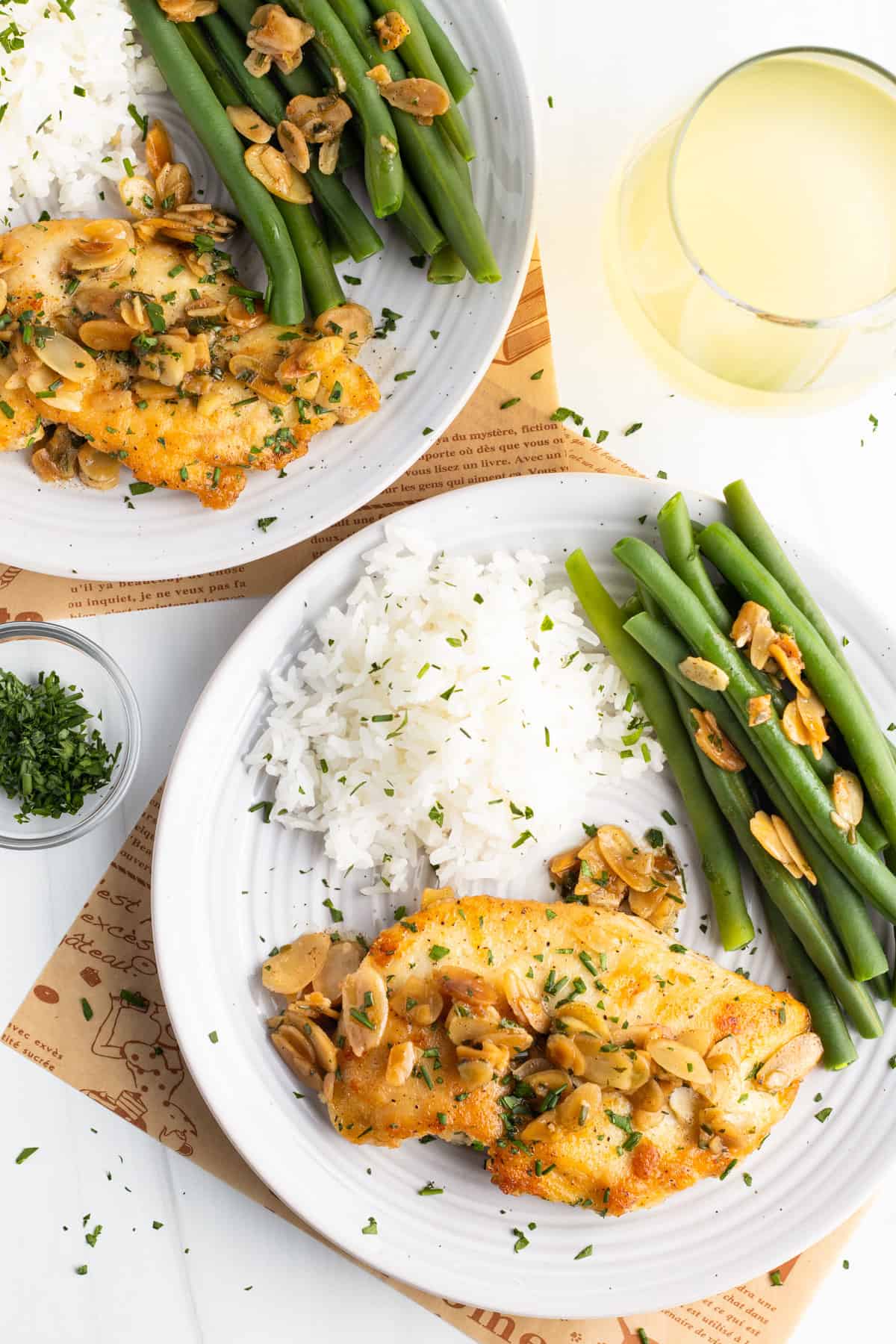 Overhead view of two plates of chicken almondine with white rice and bright green beans.