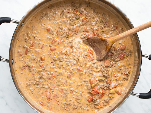 Overhead view of a large silver skillet containing the ground beef cream sauce for Rotel pasta.
