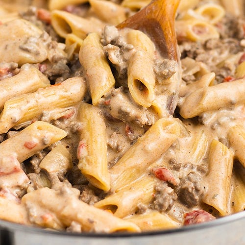 Penne pasta and ground beef in a creamy sauce, being lifted out of a large pot with a wooden spoon.