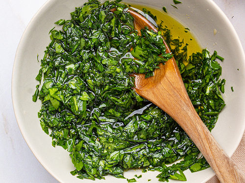 Overhead view of chimichurri mixed in a bowl with a wooden spoon.