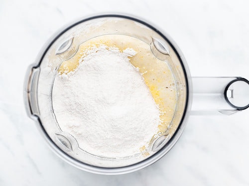 Overhead view of banana puree and instant pudding mix in a blender on a white counter.