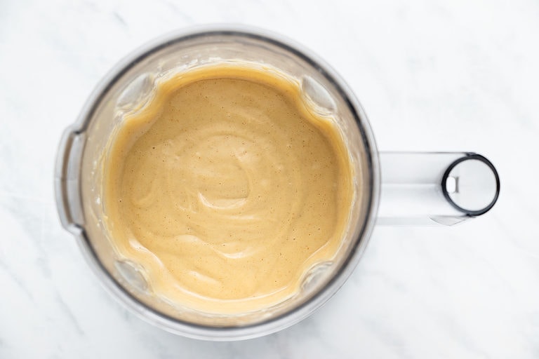 Overhead view of smooth, creamy banana pudding in a blender on a white countertop.