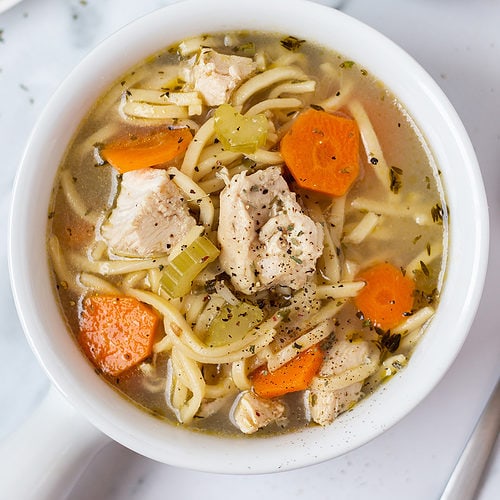 Top-down look at a bowl of chunky chicken noodle soup with broth and sliced carrots.