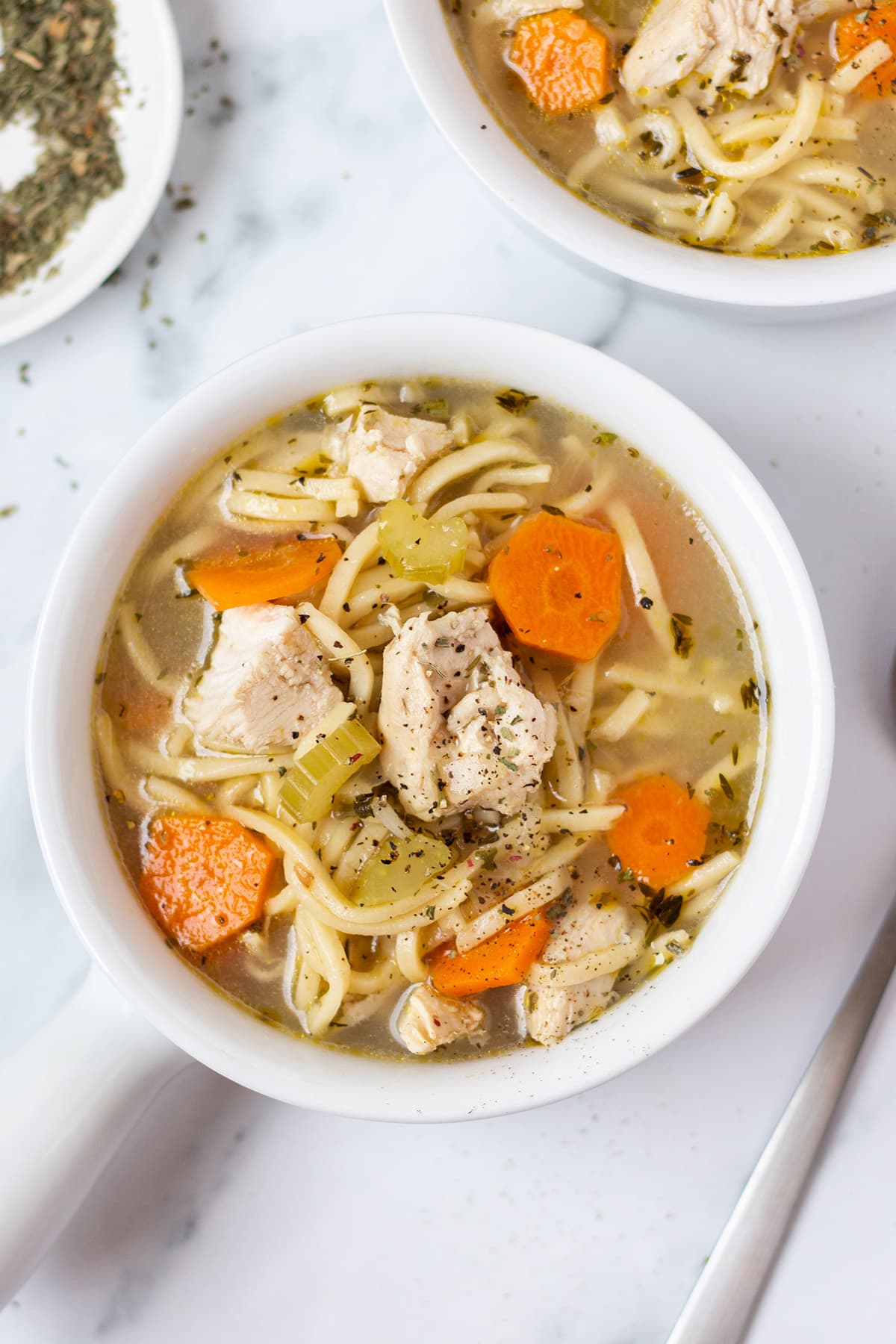Top-down look at a bowl of chunky chicken noodle soup with broth and sliced carrots.