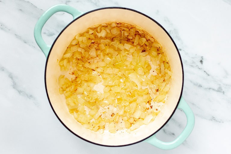 Olive oil, translucent onions, and softened garlic in a large soup pot with two handles on a marble countertop.