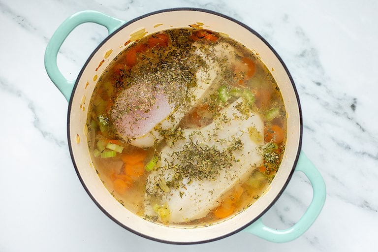 Ingredients for chunky chicken noodle soup in a large soup pot with double handles on a marble countertop.