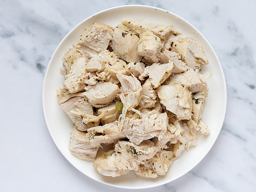 Medium chicken breasts chopped into large chunks sitting on a white plate on a marble countertop.