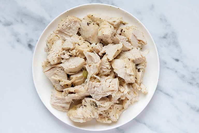 Medium chicken breasts chopped into large chunks sitting on a white plate on a marble countertop.