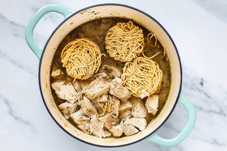 Chunky chicken pieces and 3 balls of egg noodles in a large soup pot with broth and veggies.