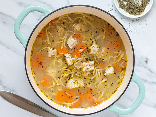 Prepared chunky chicken noodle soup in a large soup pot on a marble countertop.
