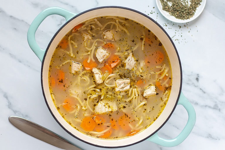 Prepared chunky chicken noodle soup in a large soup pot on a marble countertop.