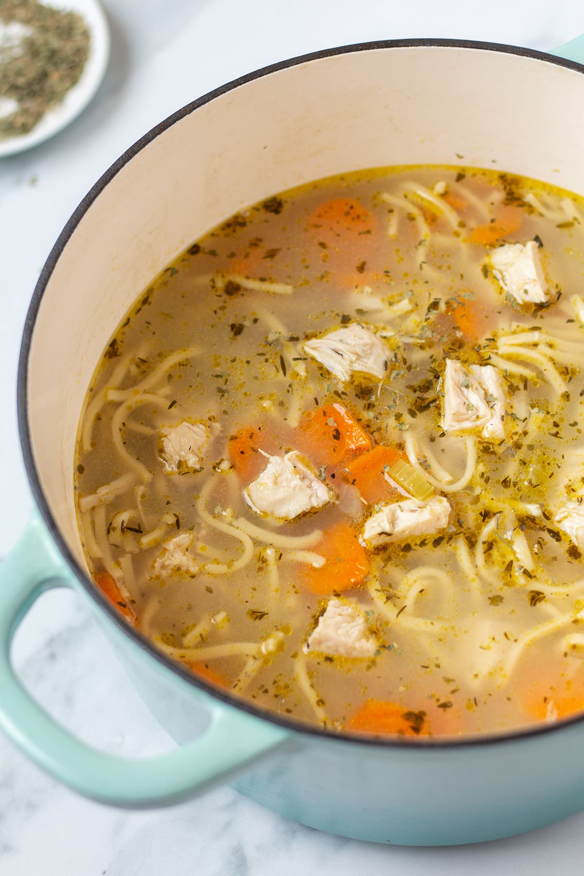 Chunky chicken noodle soup with slices of carrots in a large, heavy-bottomed soup pot with 2 handles.