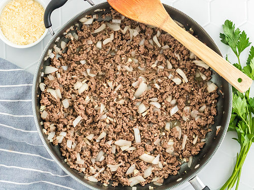 Ground beef and chopped onions in a large skillet with a wooden spoon.