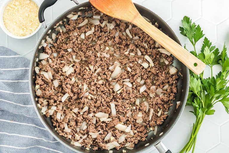 Ground beef and chopped onions in a large skillet with a wooden spoon.