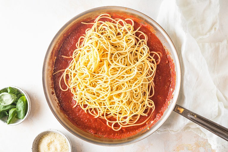 Cooked spaghetti pasta added to red sauce in a large silver skillet.