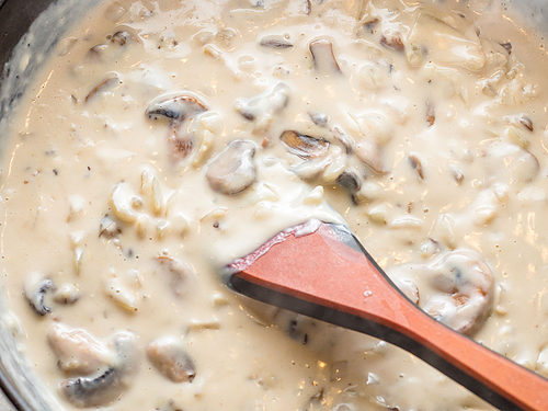Cream sauce for tuna tetrazzini in a large skillet with a wooden spoon.