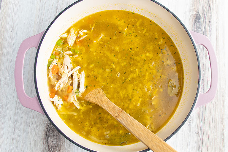 Chicken broth with shredded chicken, onions, carrots, celery, garlic, and other soup ingredients in a dutch oven.