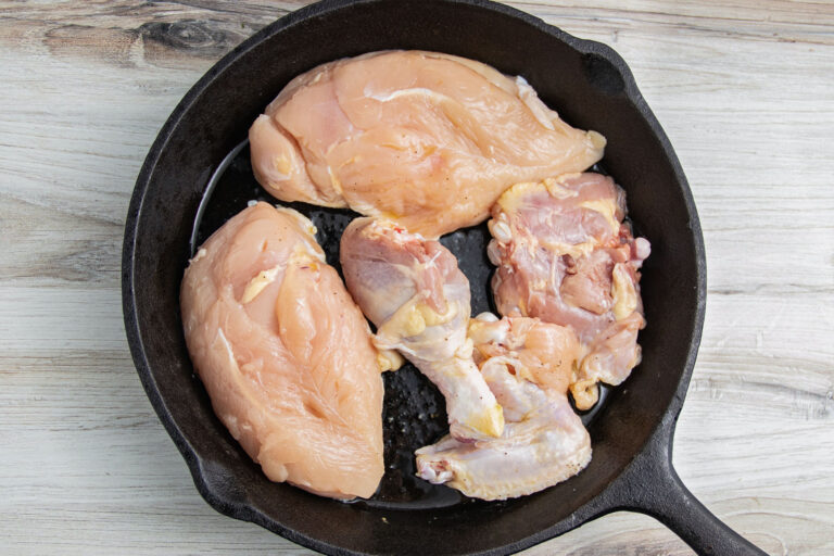 Cuts of uncooked chicken in a large cast-iron skillet.