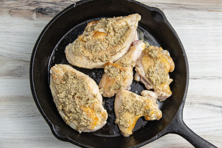 Cuts of chicken in a large cast-iron skillet, coated with parmesan garlic rub.
