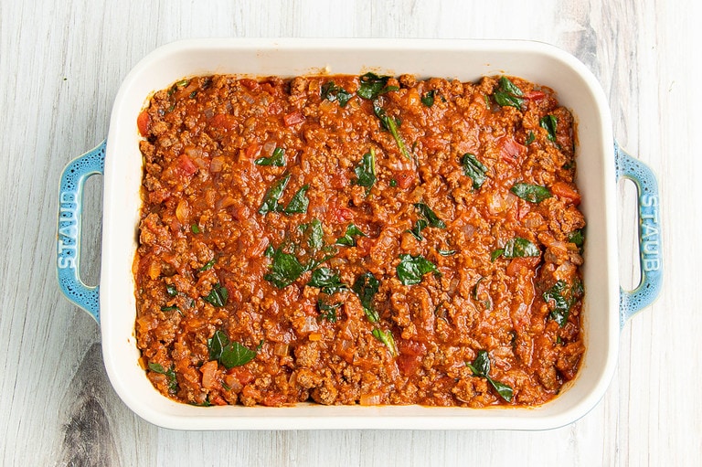 Bread covered with meat and marinara sauce on a baking dish.