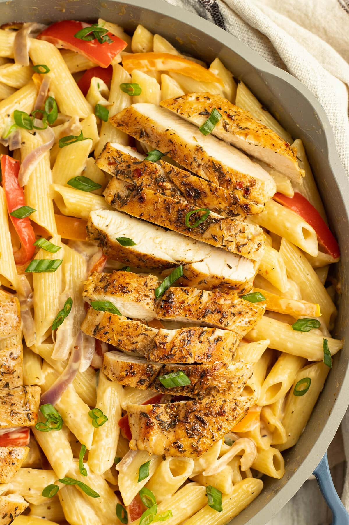Close-up of sliced jerk chicken in a saucepan with alfredo pasta.