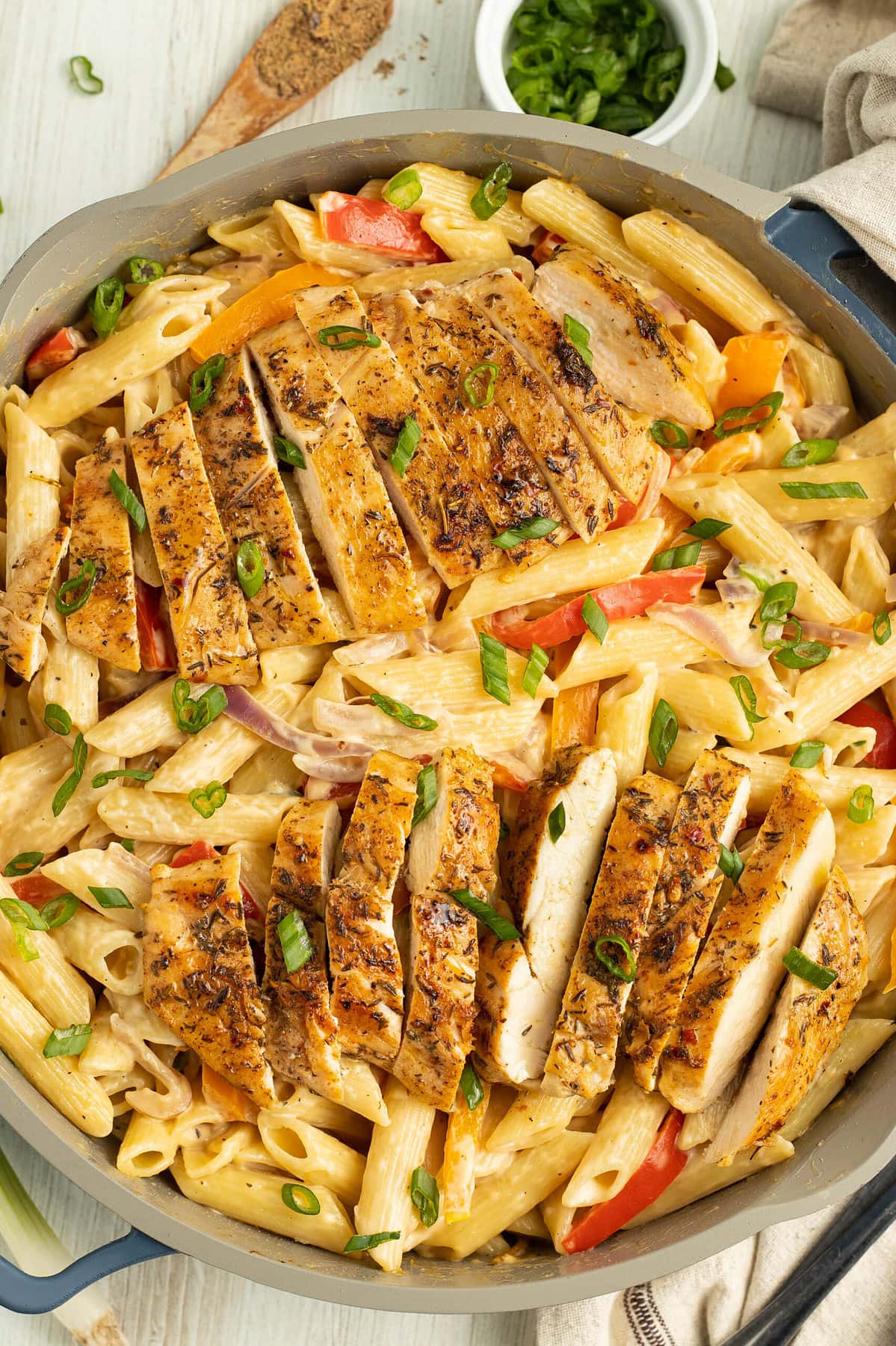 Top-down look at jerk chicken alfredo in a large silver skillet with pasta.