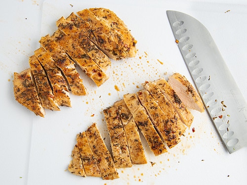 Sliced jerk chicken cutlets on a cutting board.