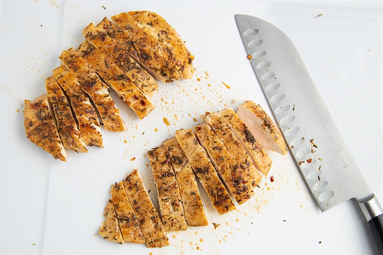 Sliced jerk chicken cutlets on a cutting board.