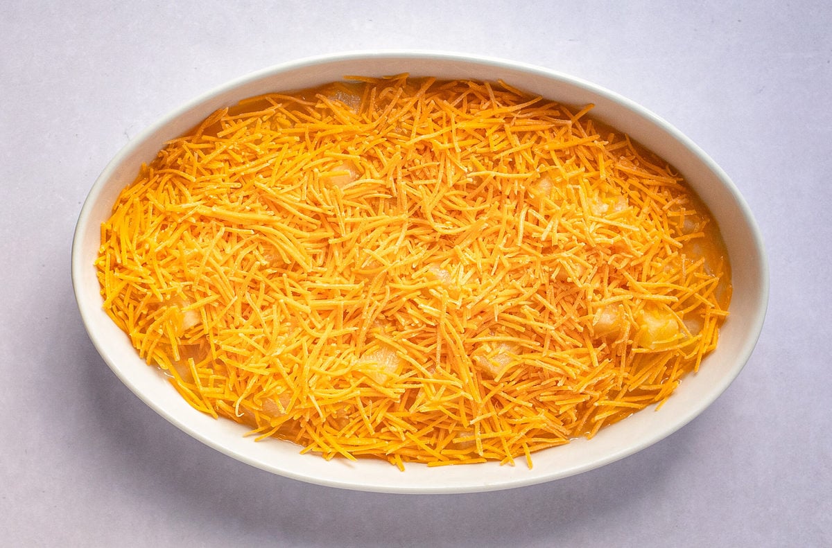 Shredded sharp cheddar cheese on top of the pineapple casserole filling in a casserole dish.