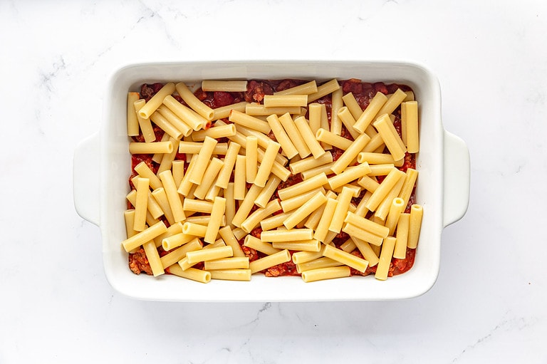 Boiled ziti covering meat sauce in rectangular baking dish.