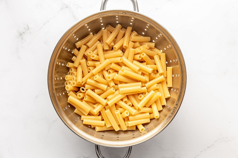 Boiled ziti noodles in a silver colander.