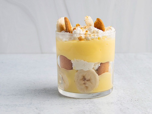 Side view of a banana pudding cup layered with bananas, pudding, whipped cream, and vanilla wafers.