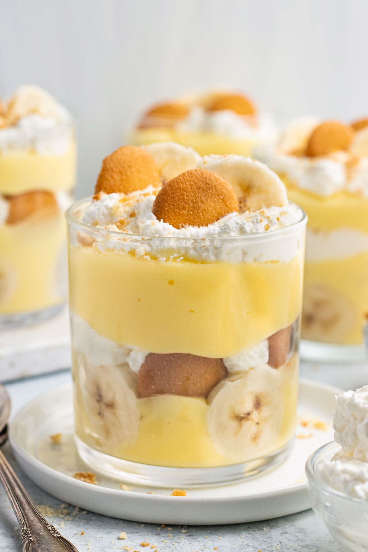 Glass cups of banana pudding layered with homemade whipped cream, banana slices, and vanilla wafers.