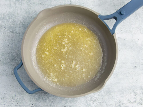 Melted butter and minced garlic in a large grey skillet.
