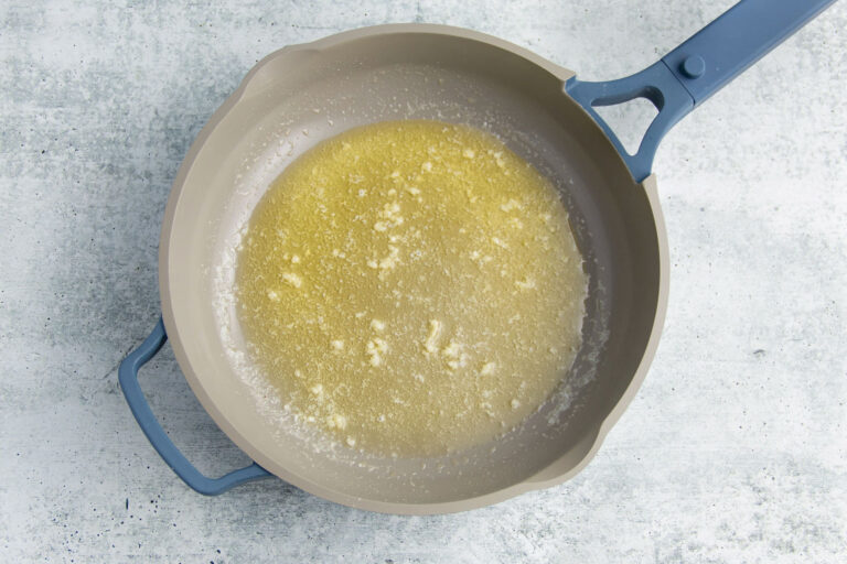 Melted butter and minced garlic in a large grey skillet.