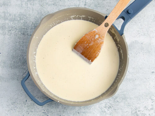 Heavy cream, butter, and garlic in a large skillet with a large wooden spoon.