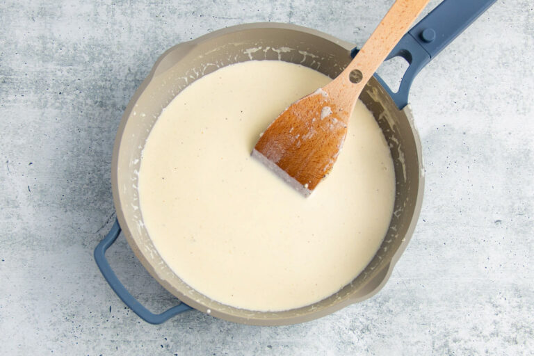 Heavy cream, butter, and garlic in a large skillet with a large wooden spoon.