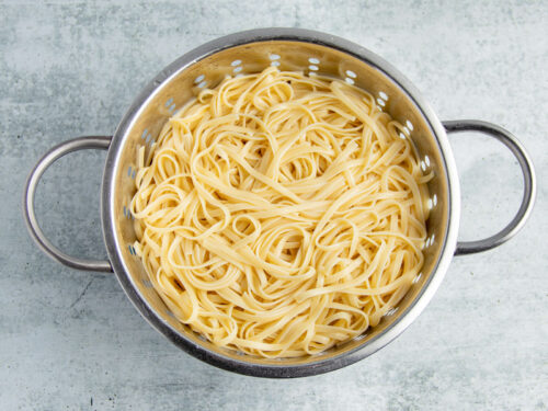 Cooked linguine in a silver colander.