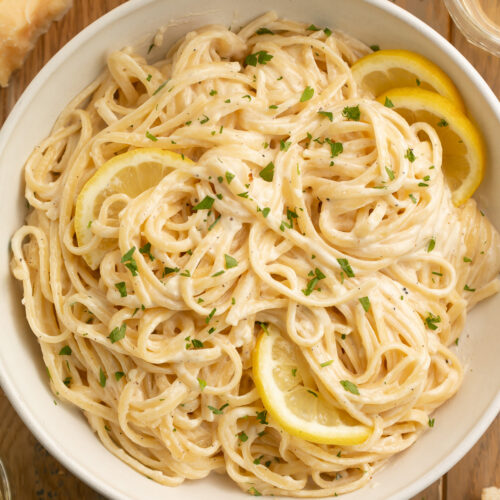 A bowl of lemon pepper pasta made with spaghetti noodles and garnished with lemon wedges.