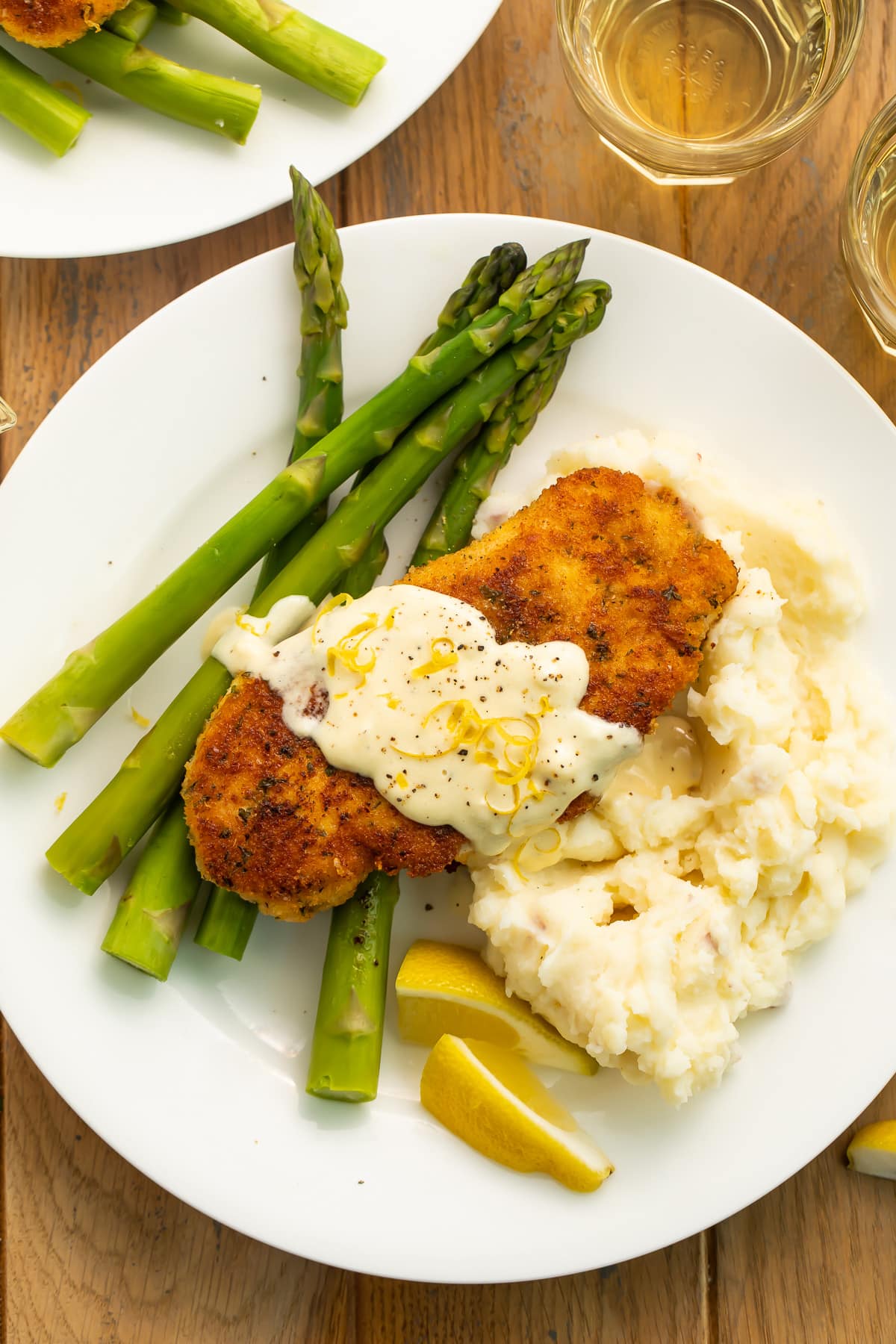Close up of a plate of chicken costoletta served with asparagus and lemon wedges on a white plate.