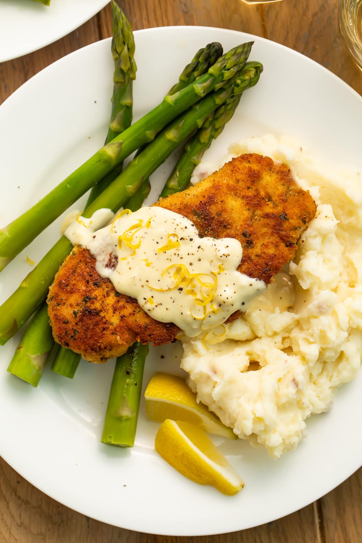 Breaded chicken costoletta topped with a cream sauce on a white plate with bright green asparagus.