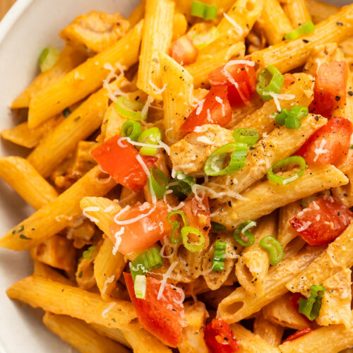 Close-up over copycat Firebirds' chicken pasta topped with diced tomatoes and chopped green onions in a large bowl.
