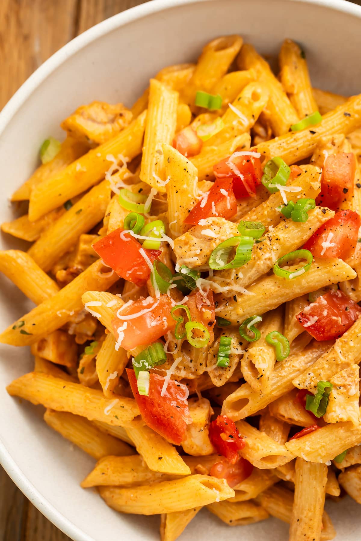Close-up over copycat Firebirds' chicken pasta topped with diced tomatoes and chopped green onions in a large bowl.