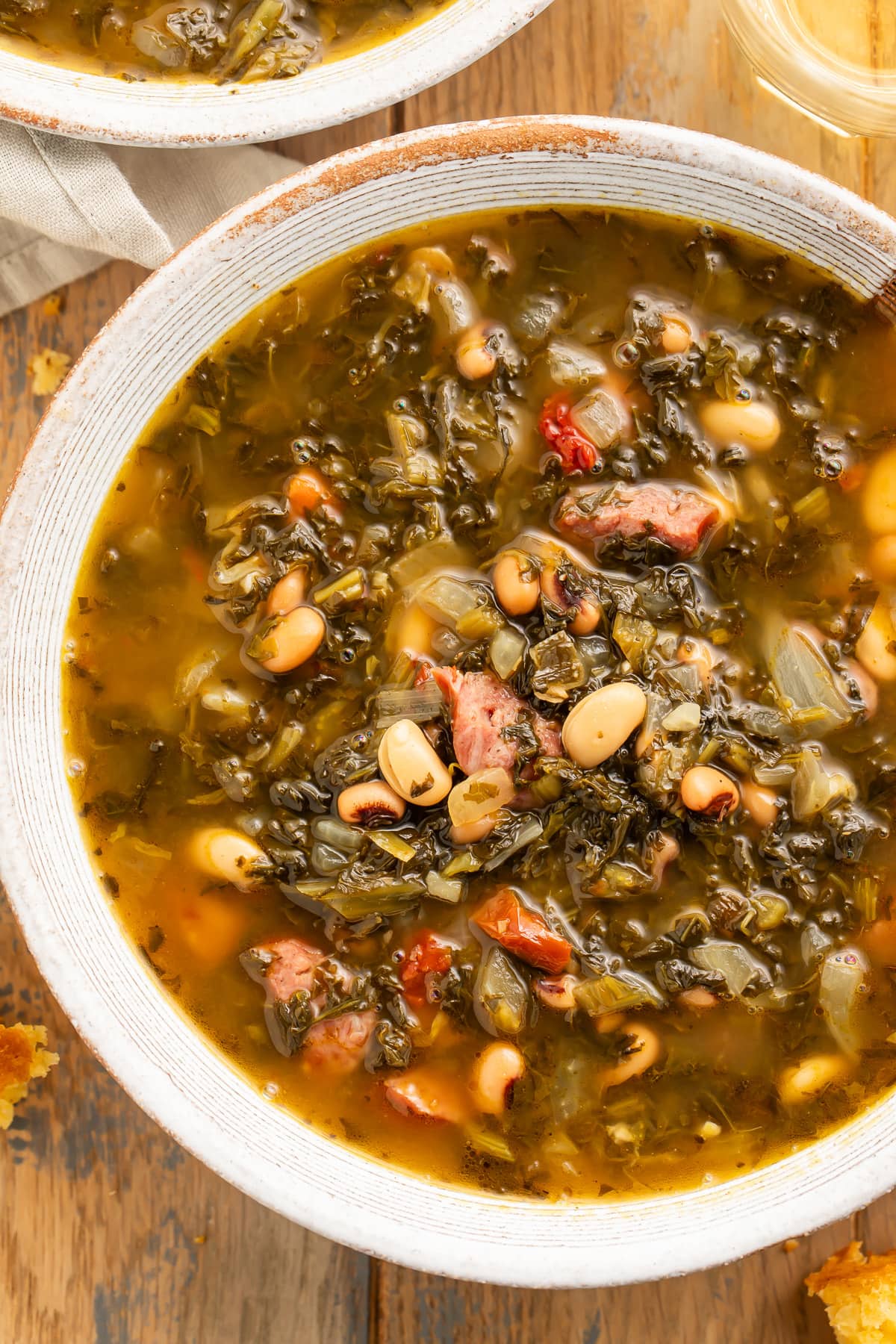 A large white soup bowl holding dark brown turnip green soup with turnip greens, smoked sausage, and beans.