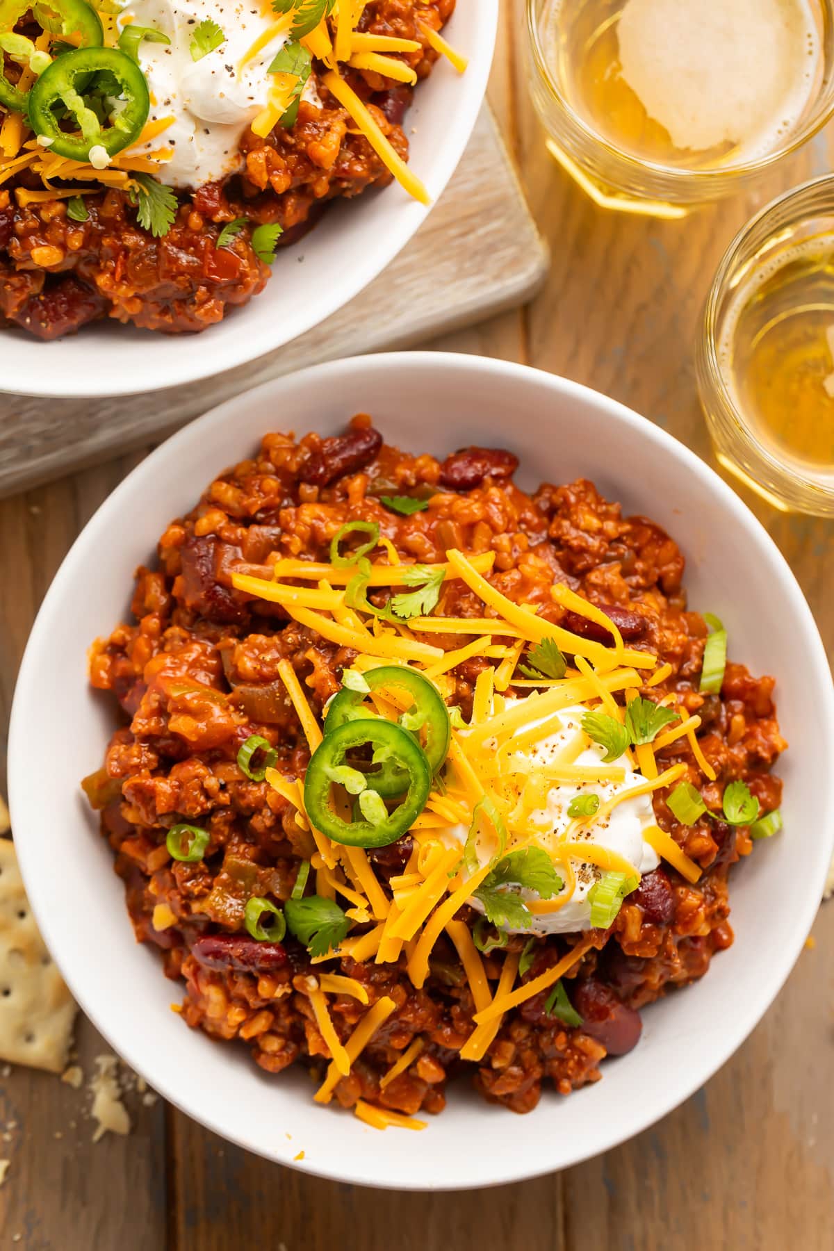Overhead view of two large white bowls containing deep red chili, mixed with rice and topped with sour cream and shredded cheese.