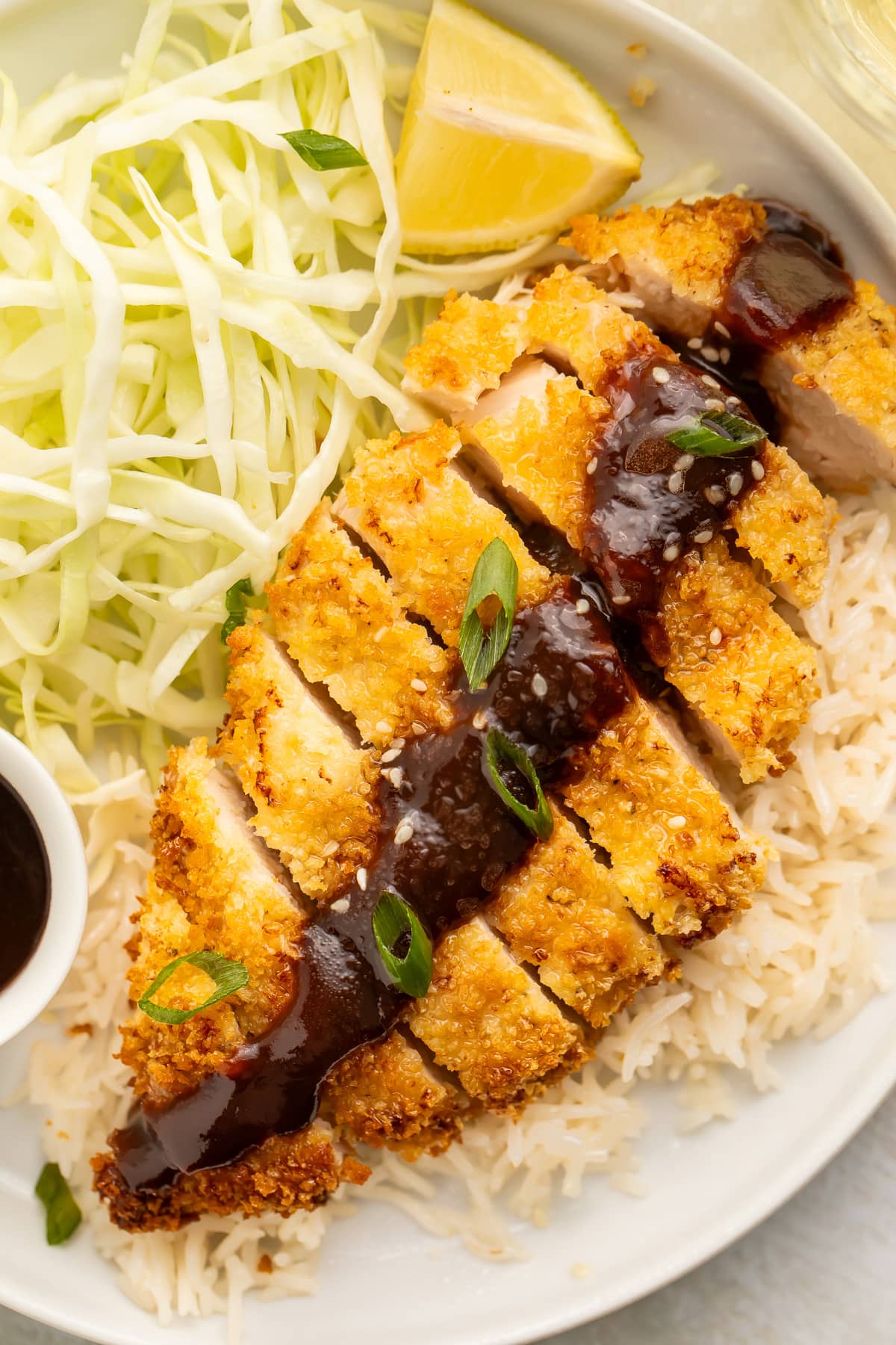 Close-up of chicken katsu, cooked in the air fryer, plated with a salad and a line of sauce.